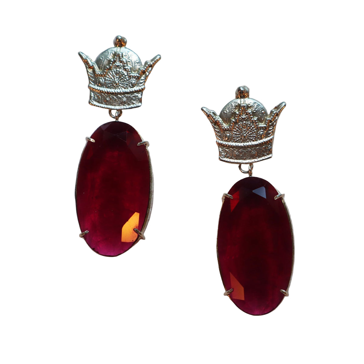Pair of earrings with red gemstones and silver crown-like tops on a textured white background